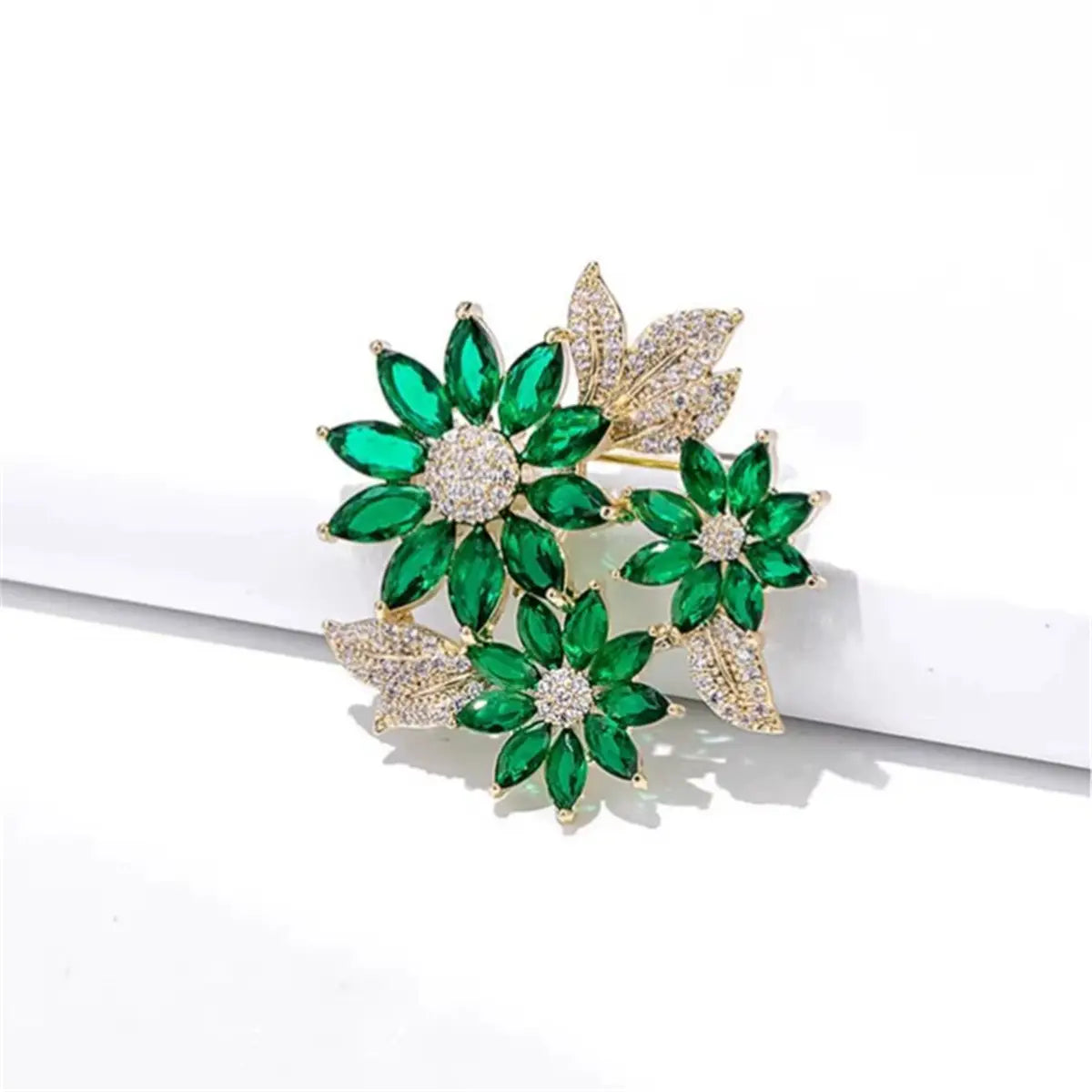 A sparkling green floral rhinestone brooch pin featuring three emerald-green marquise-cut stones and gold diamond-encrusted leaves arranged in a bouquet design.