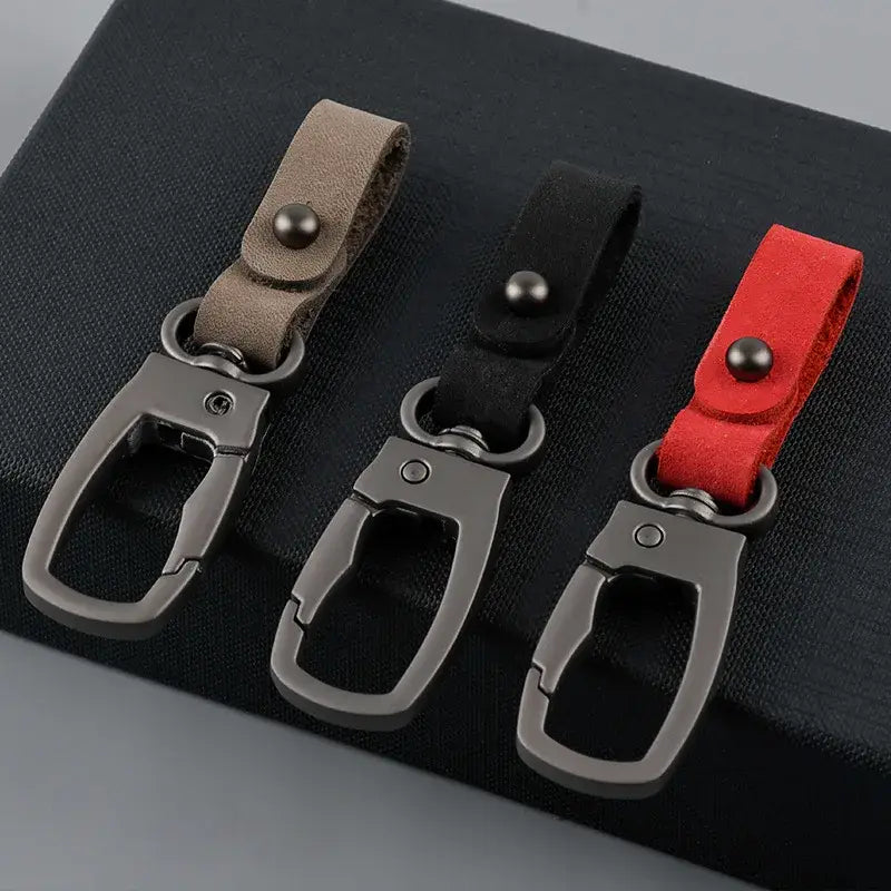 Three leather keychain car key holder organizer charms with textured leather straps in beige, black, and red.