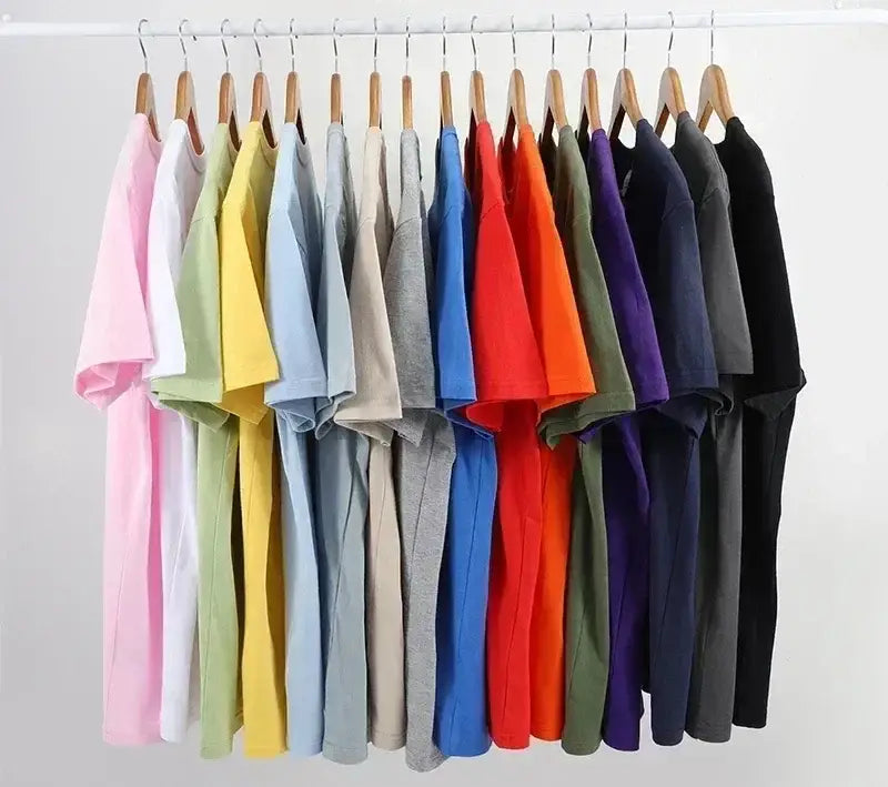 Une rangée de t-shirts vintage à motif de voiture de muscle en coton uni et coloré, suspendus à des cintres en bois.
