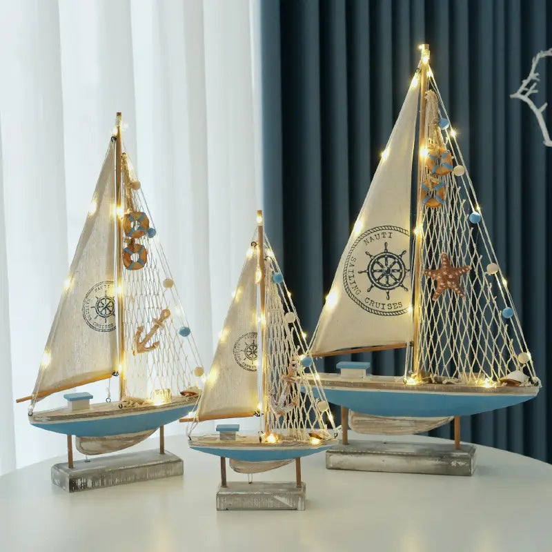 Drei dekorative LED-Segelboote im mediterranen Stil aus Holz mit blauen Rümpfen und segelfarbener Segel in Creme, verziert mit maritimen Motiven und Lichterketten für die Wohnraumdekoration.