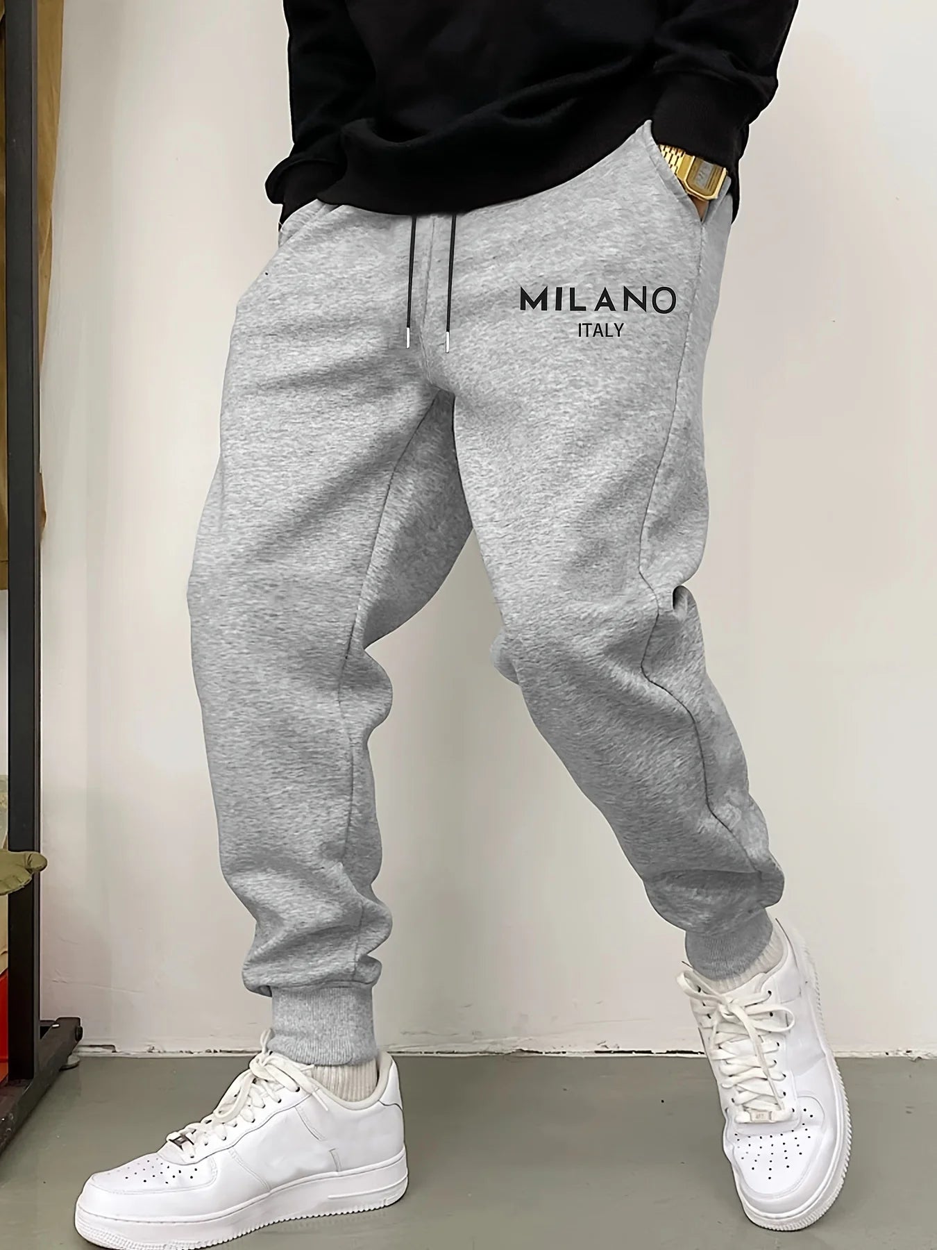 Graue melierte Fleece-Jogginghosen für Herren mit in Schwarz auf der linken Oberschenkelseite besticktem Milano, Italien.