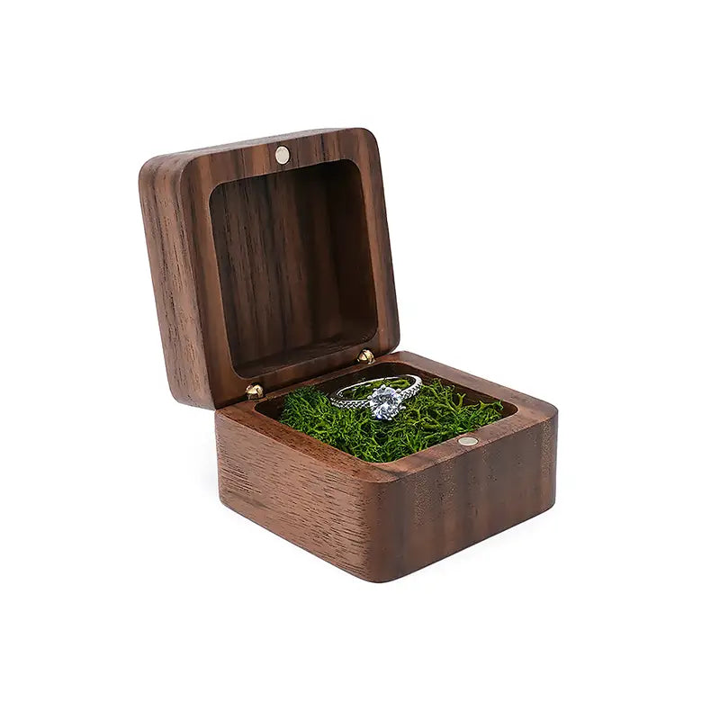 Boîte à bague en bois foncé pour proposition de mariage, présentoir pour bague d’engagement, présentant une bague solitaire en argent sertie d’un diamant reposant sur de la mousse verte à l’intérieur.