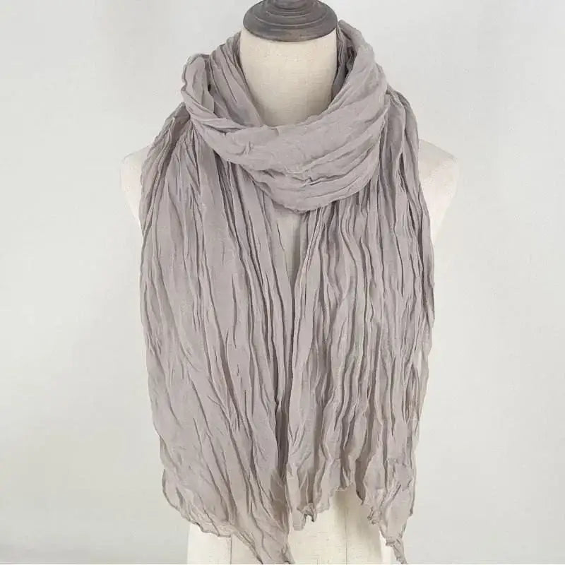 Una bufanda de algodón lino gris claro suave para mujer, elaborada con tela transpirable, drapeada con elegancia alrededor del cuello de un maniquí.