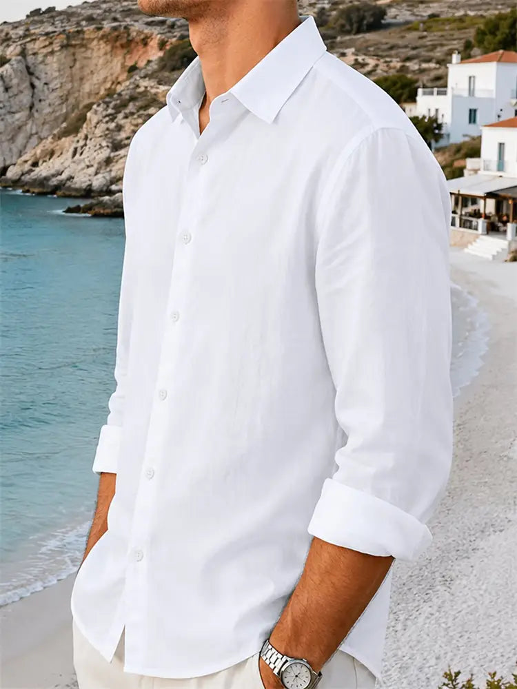 Un homme portant une chemise blanche pour homme en coton et lin à manches longues, avec poignets retroussés, se tenant près de la plage.