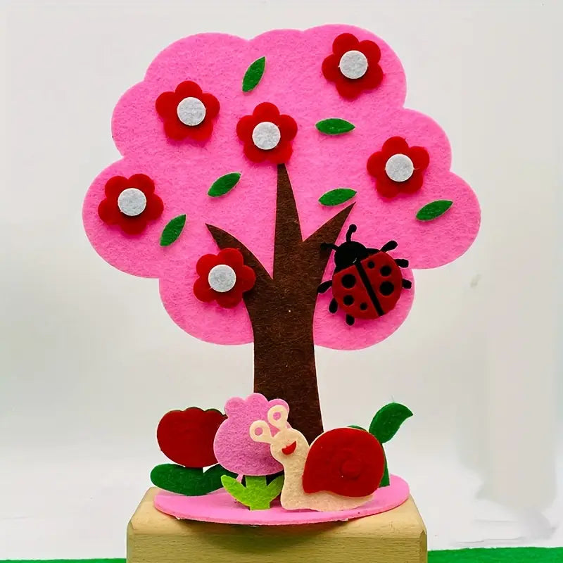 kit de manualidades estacionales de árbol de fieltro tipo diy que incluye un árbol de fieltro rosa vibrante adornado con flores rojas, hojas verdes, una mariquita en su tronco y un caracol debajo.