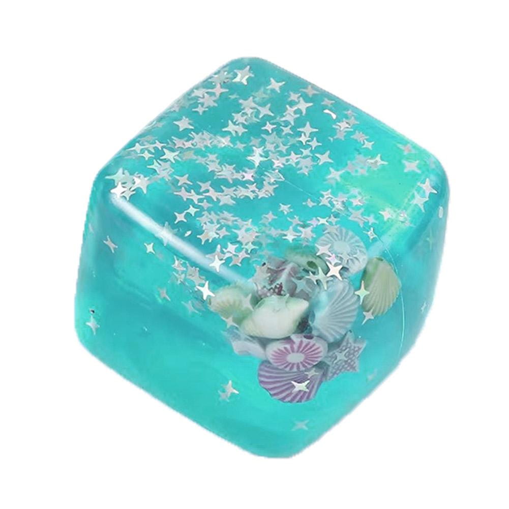 Un cube sensoriel à effet anti-stress pour l’océan en turquoise translucide, rempli de confettis argentés en forme d’étoiles et de coquillages assortis, conçu comme un cadeau attentionné.