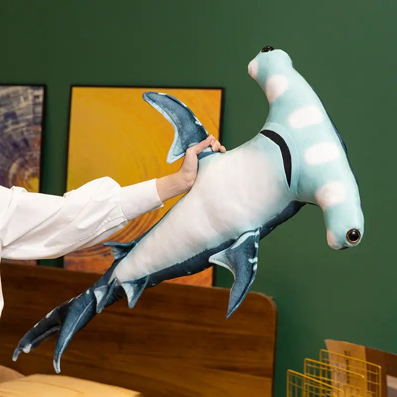 A plush hammerhead shark pillow soft toy in light blue and white with detailed stitching on fins and eyes.