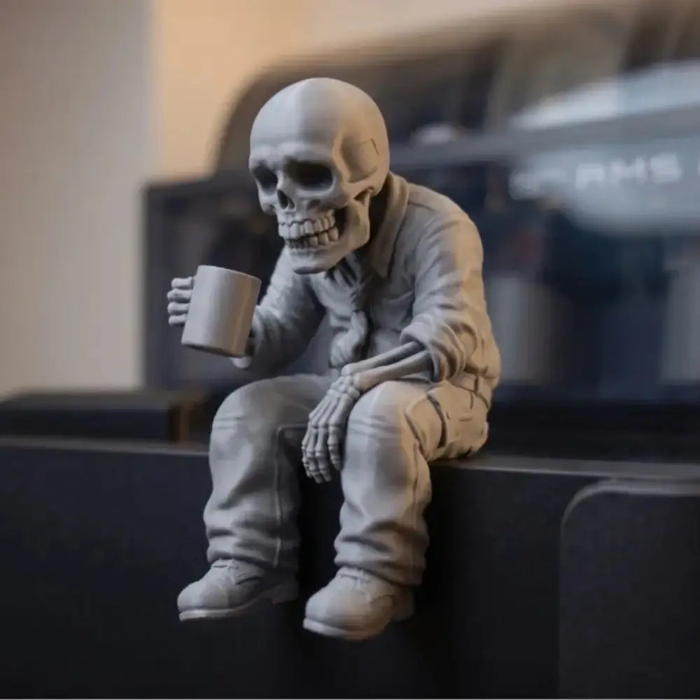 A gray skeleton figurine dressed in casual attire seated and holding a mug is a skeleton coffee desk figurine office ornament.