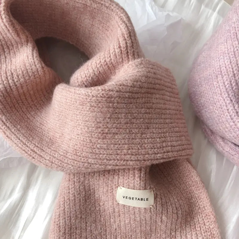 女性用のソフトピンクのリブ編みカシミヤ冬用ストールで、居心地のよい厚手の質感と小さなベジタブルのブランドタグ付き。