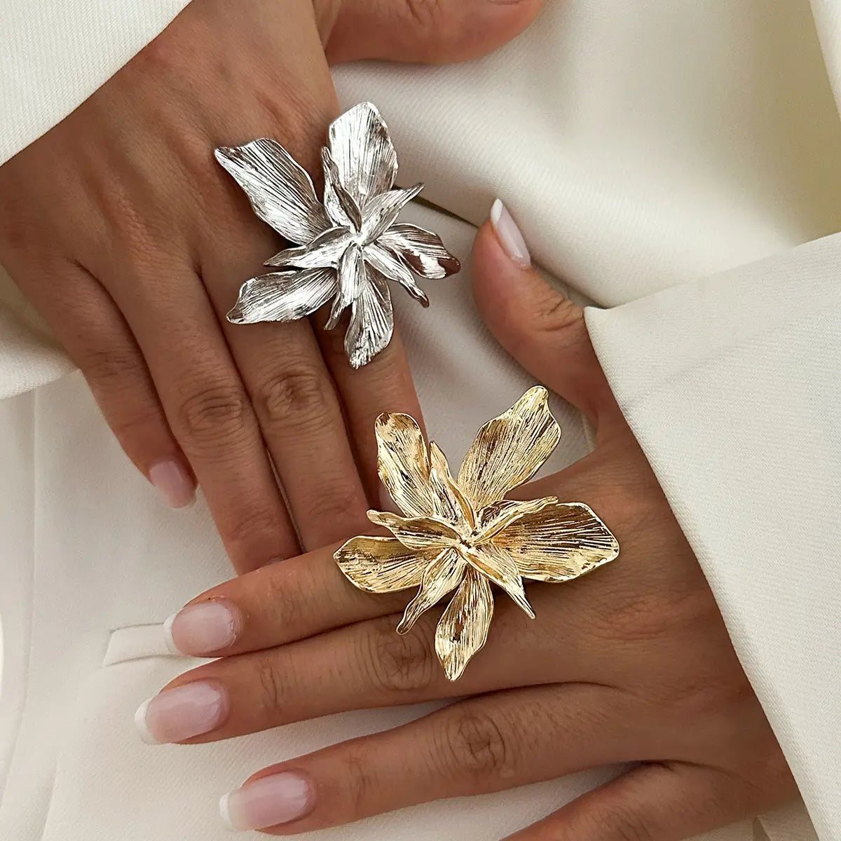 A hand with neatly manicured nails wearing two adjustable double layer flower rings in ornate silver and gold metal.