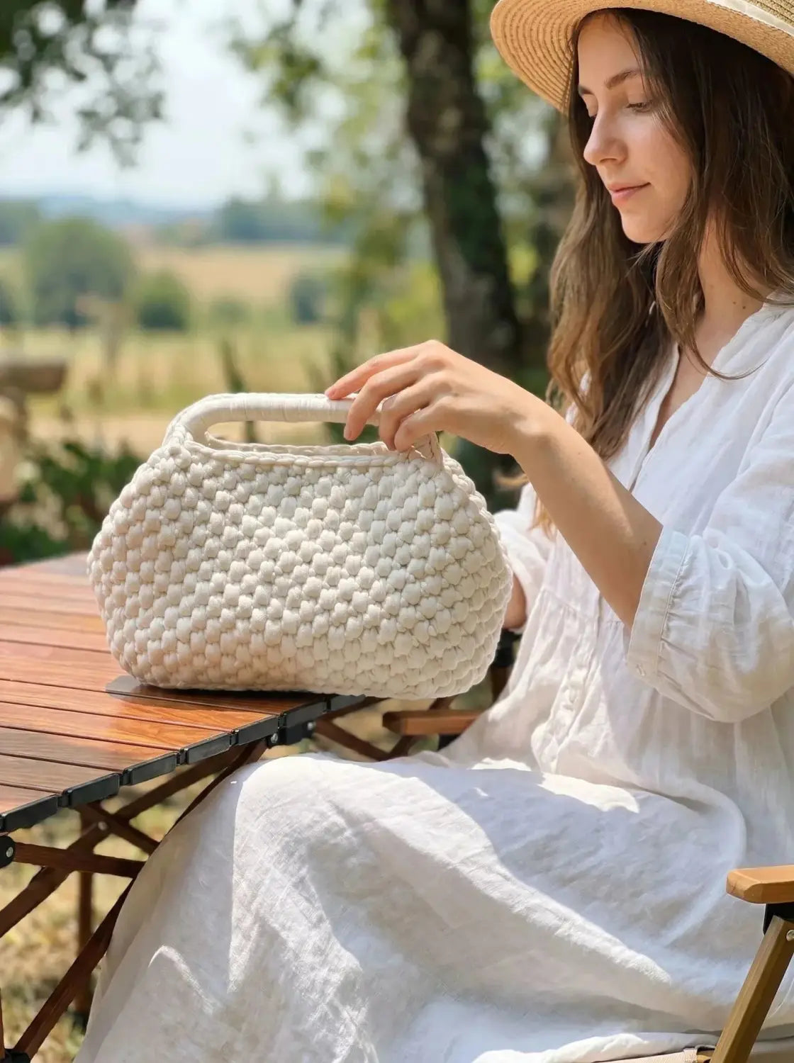 Un bolso bandolera color crema de punto grueso tejido a crochet, con forma redondeada y asa resistente, diseñado como bolso para vacaciones de playa.