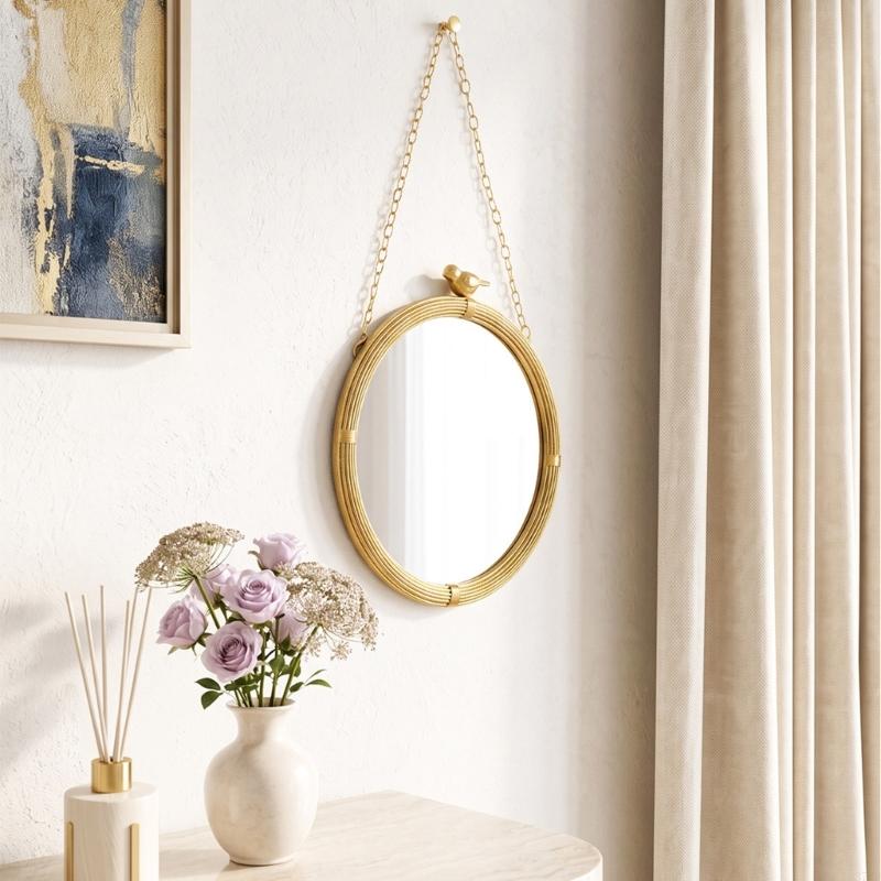 Miroir décoratif ovale à la finition dorée, à monture en résine de rotin tressé et à une petite touche décorative représentant un oiseau, suspendue par une chaînette assortie, conçue pour une décoration murale intérieure.