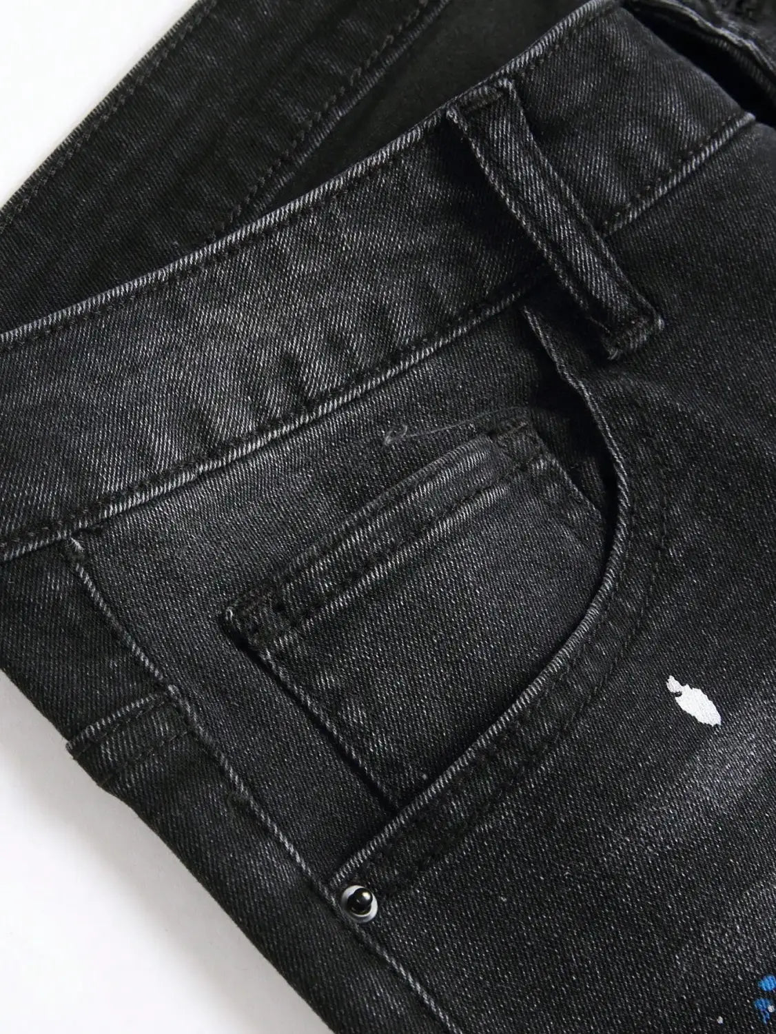 Jeans denim noirs skinny extensibles déchirés Y2K pour hommes, offrant un aspect vieilli et délavé, avec des accents discrets d’éclaboussures de peinture blanche.