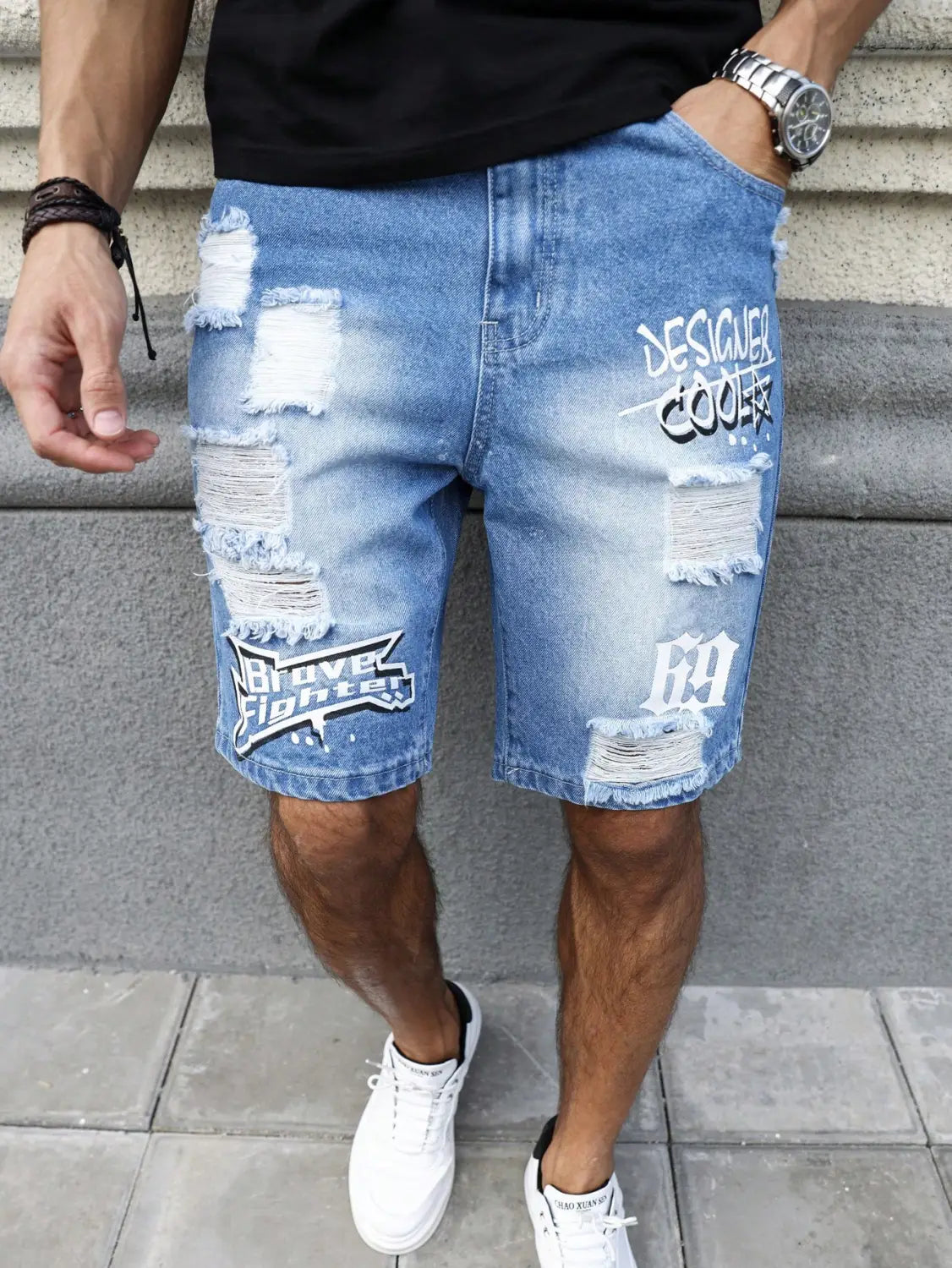 Shorts en jean pour hommes, effet délavé clair, avec des patchs déchirés et un aspect vieilli, et une typographie blanche style graffiti comprenant les logos « designeer cooler » et « brove fighter », idéals pour une tenue d’été.