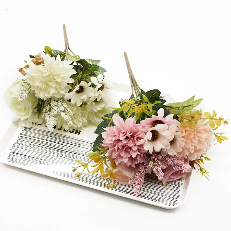 造花のバラのウェディングブーケが2点。1点は柔らかな白とクリーム系のトーンで、繊細なグリーンが添えられており、もう1点はブラッシュピンク、淡いピーチ、黄色の花を淡い色合いでまとめ、紫の枝でアクセントを加えています。