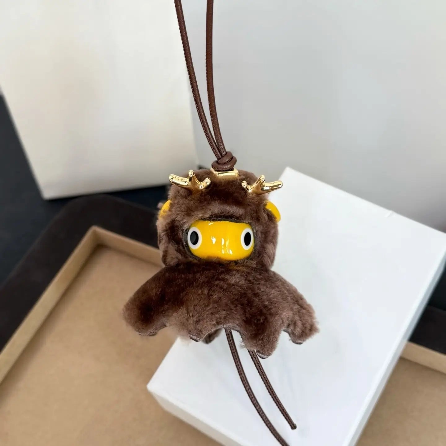 Llavero colgante para bolso con encanto de animales de cuero marrón tipo peluche, con astas doradas y un rostro amarillo, en un estilo de diseñador tierno.