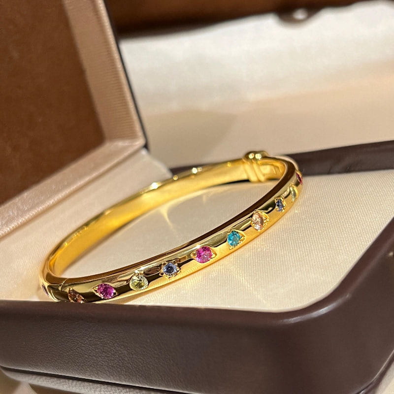 Ein Armreifarmband aus goldfarbenem Multigemsteinschmuck mit einem eleganten, polierten Design und farbigen Edelsteinen.