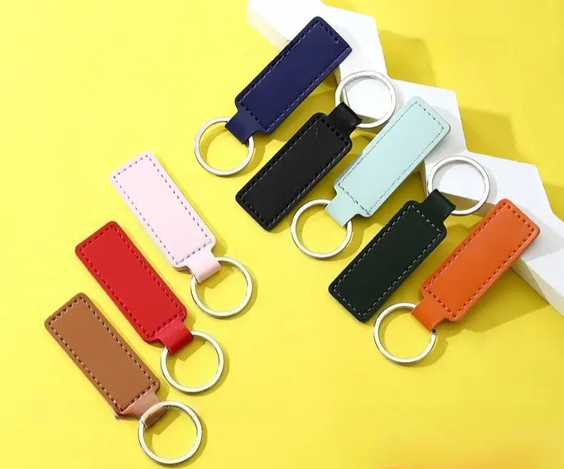 a collection of customized leather keychains in various colors including navy black light blue red pink brown and orange displayed as rectangular strips