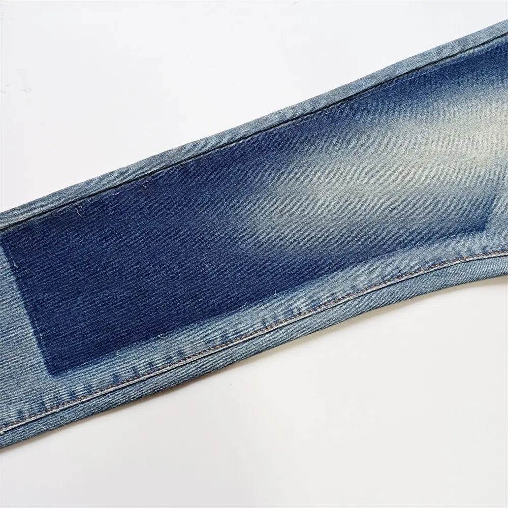 Gros plan sur un tissu en denim bleu délavé, avec coutures visibles et un empiècement plus foncé cousu sur la couture, pour jeans skinny déchirés, effet délavé rétro vintage bleu.