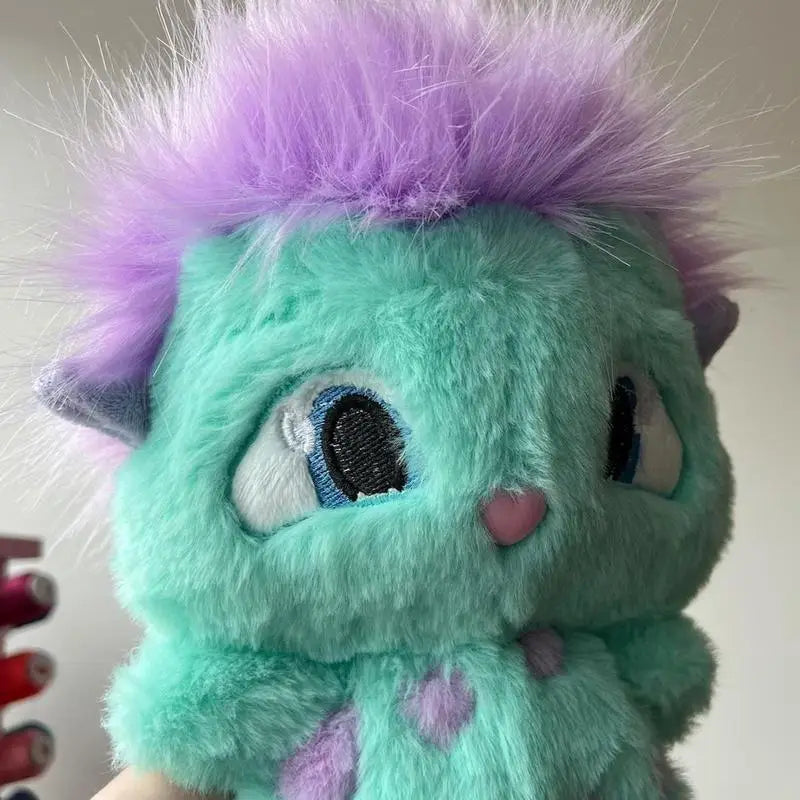 a plush turquoise bibble plush toy featuring spiky purple fur embroidered blue eyes and a pink nose as a cute stuffed anime doll