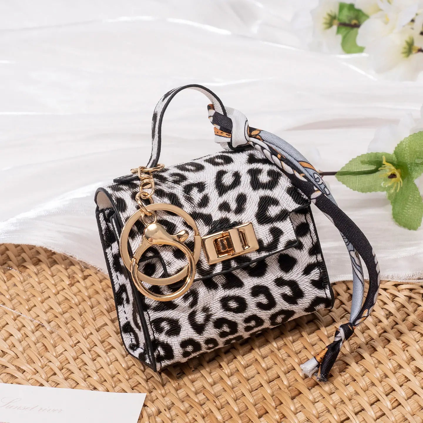 Miniature handbag keychain with silk scarf featuring a black and white leopard print fabric, gold-tone hardware, a matching knotted strap, and an attached keychain with two interlocking rings.