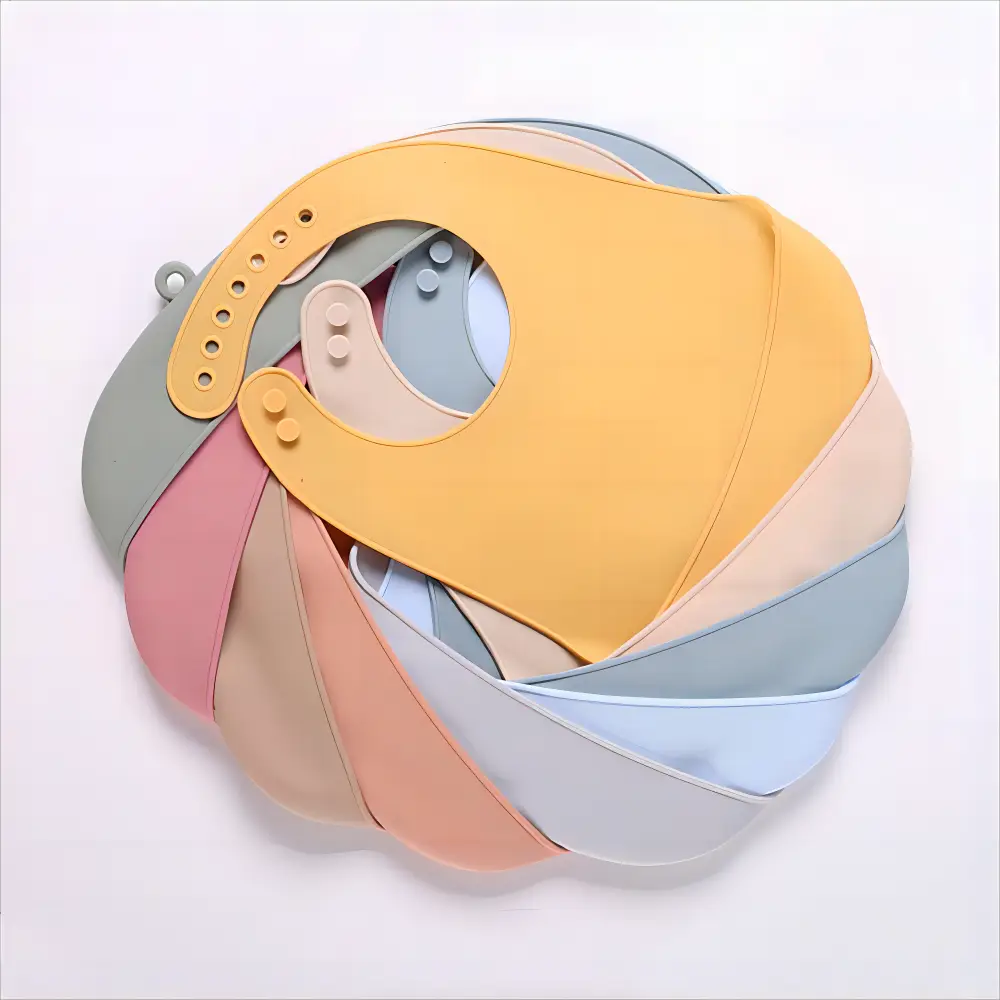 Eine Kollektion pastellfarbener Silikon-Lätzchen für Babys in sanftem Gelb, Rosa, Blau und Grau, hergestellt aus wasserfestem, verstellbarem Silikon für Säuglinge