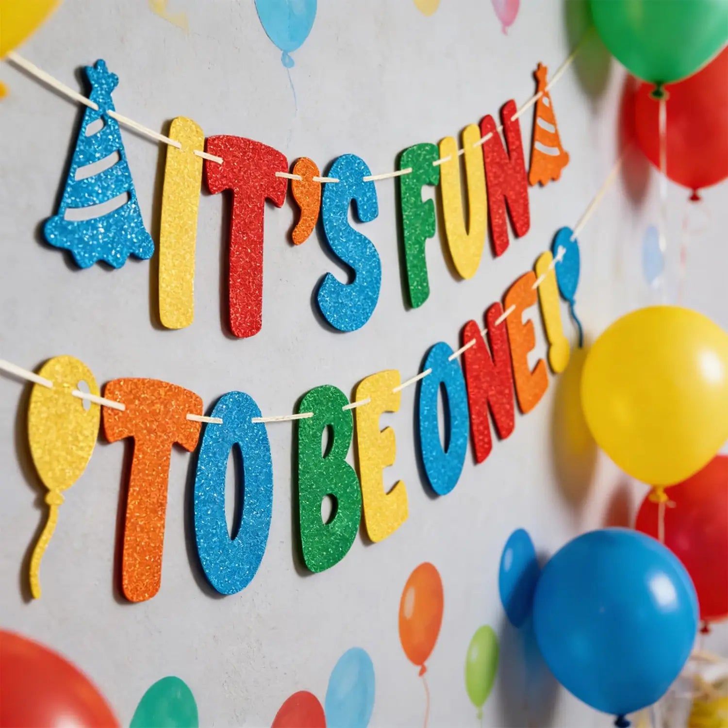 Glitzernde Geburtstagbanner-Partydekoration zum ersten Geburtstag mit einem farbenfrohen glitzernden Banner „Es macht Spaß, eins zu sein“ mit Partyhütchen- und Ballon-Ausschnitten.
