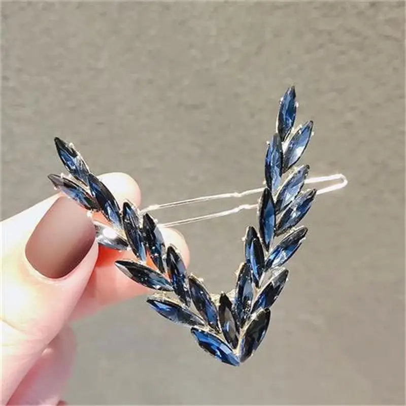 A delicate silver crystal v shape hair clip set adorned with deep blue faceted crystal leaves arranged in a graceful v shape.