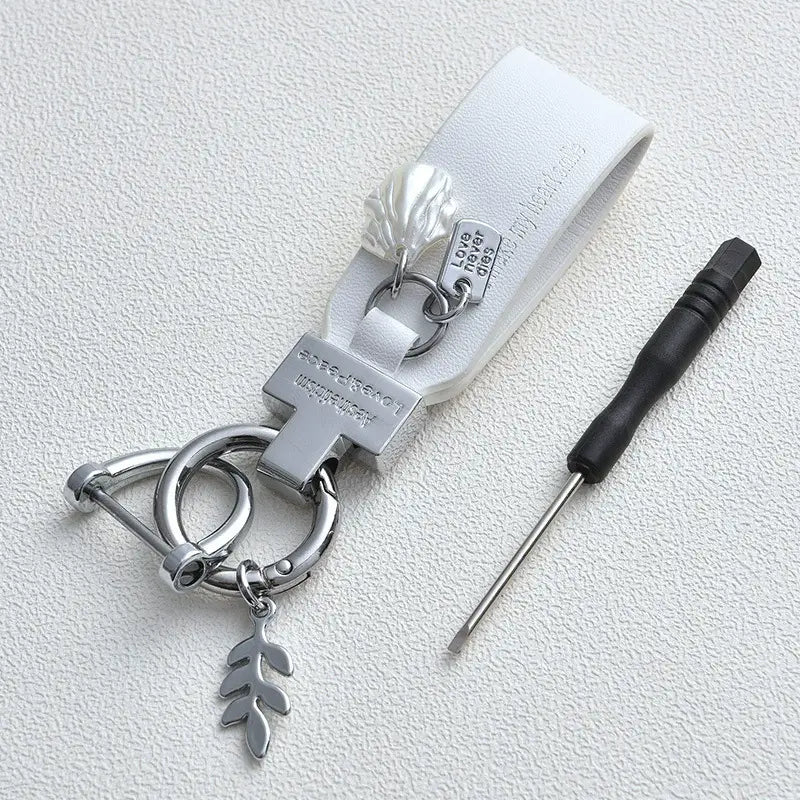 Llavero de piel blanca con acentos metálicos plateados, colgante con forma de concha y dijé en forma de hoja, diseñado como un llavero antirrobo estilo francés para automóvil.