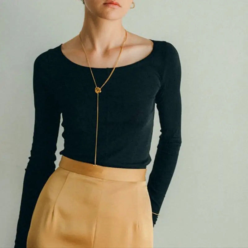 Haut noir à manches longues côtelées avec encolure carrée, associé à un collier pendentif à superposition géométrique doré pour femmes.