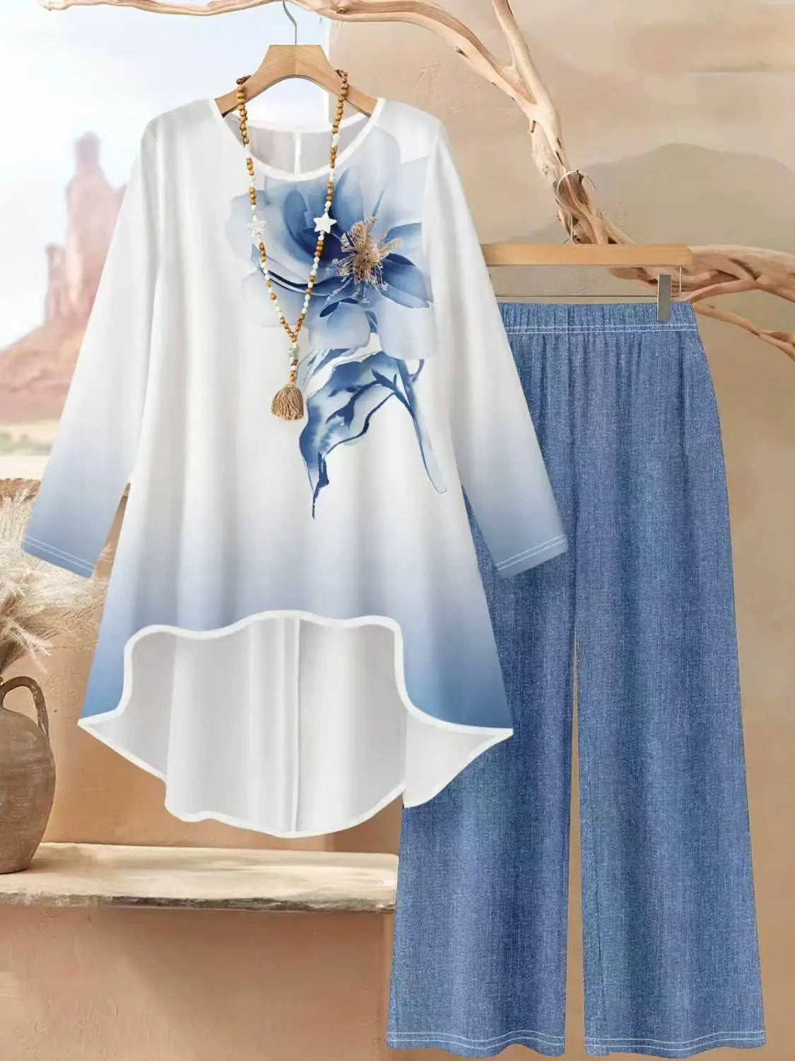 Eine fließende Bluse mit weißem und blauem Farbverlauf sowie großem Blumendruck auf der Vorderseite, die neben dazu passenden weitem Jeans mit Blumendruck in einem zweiteiligen Outfit mit weitem Bein hängt.