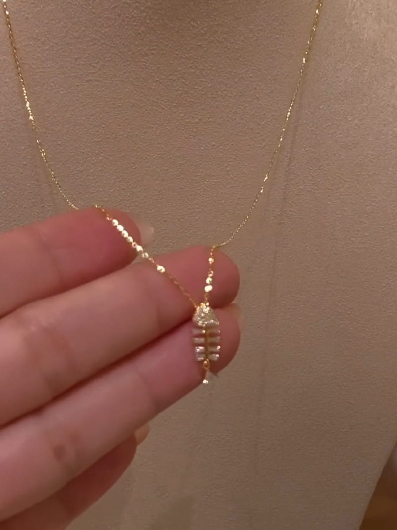 A delicate gold chain necklace with a small intricately designed fishbone pendant adorned with sparkling clear stones in the crystal fishbone gold necklace pendant jewelry collection.