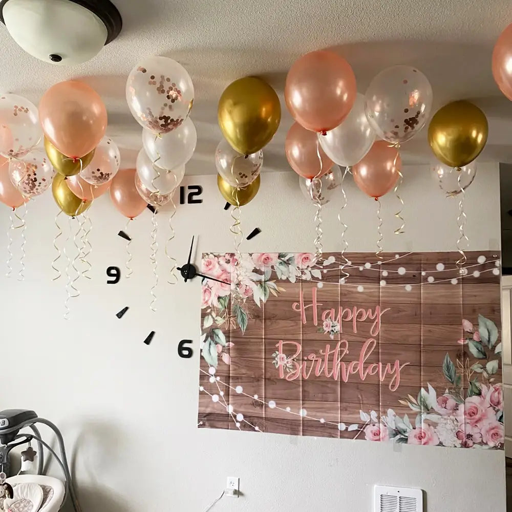 Eine dekorative Happy-Birthday-Wandgirlande mit rustikaler Holzstruktur und pinkfarbenen floralen Akzenten als Teil einer Partyddeko aus dem Roségold-Konfetti-Ballonset