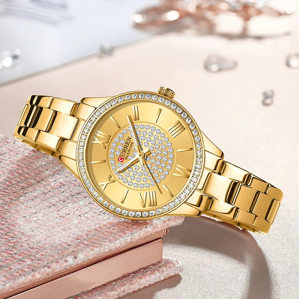 Curren women stainless steel crystal quartz watch in gold tone with diamond-studded bezel and face featuring roman numerals on a polished metal bracelet.