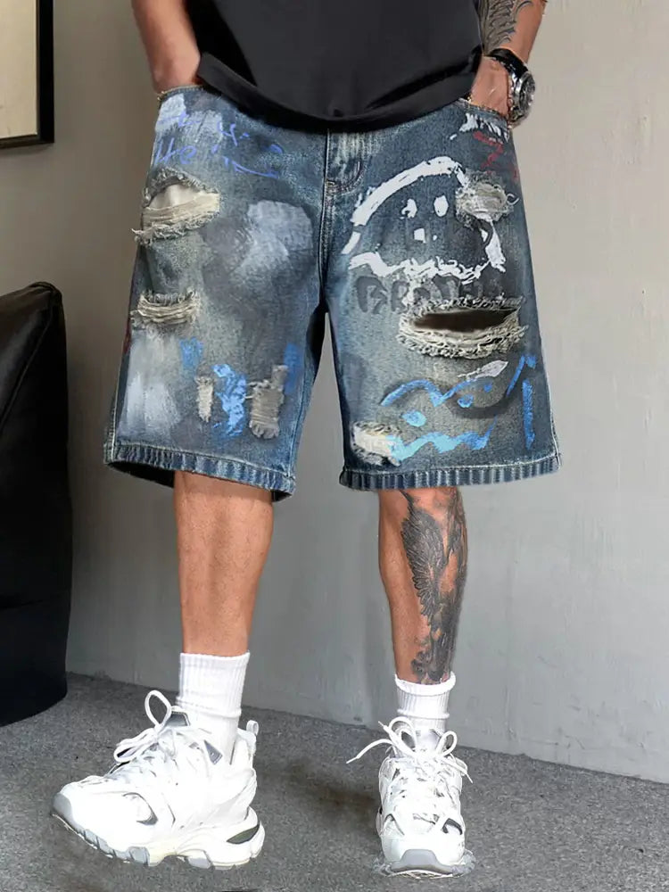 メンズ向けグラフィティ風フェイスデザインのダメージ加工ブルーデニムショートパンツ。裂けた生地と色あせたウォッシュが特徴です。