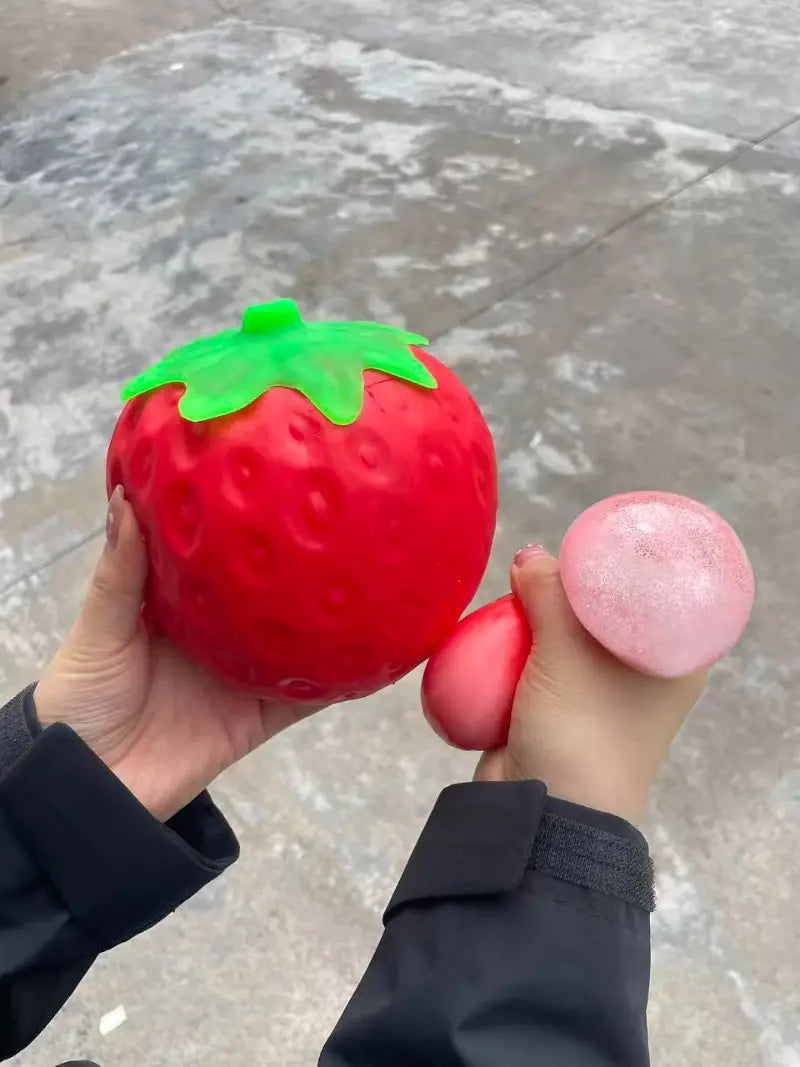 Jumbo strawberry slow rising sensory fidget toy in red with green leafy top shaped as a stress ball.