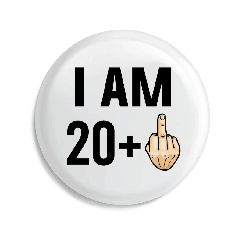 un badge de broche émaillé circulaire blanc avec du texte noir indiquant « j’ai 20 ans et plus » et une main dessinée faisant le geste du doigt d’honneur, conçu comme un cadeau amusant d’anniversaire marquant une étape d’âge.