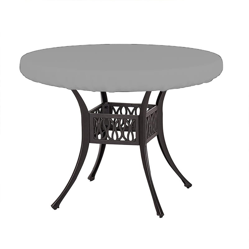 Funda de mesa de tejido impermeable gris, colocada sobre una mesa de patio de metal oscura, con patas curvadas ornamentales y una base calada para uso en jardín al aire libre.