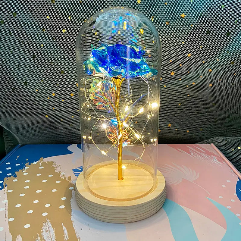 Eine leuchtend blaue Rose mit goldenem Stiel, umschlossen in einer klaren Glaskuppel, beleuchtet von zarten LED-Feenlichtern, für ein „Eternal Gold Rose Glass Dome Led Light Gift“