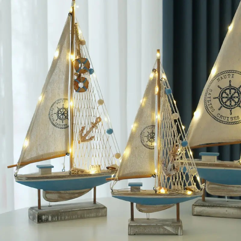 Deko im mediterranen Stil aus Holz mit LED-Licht für ein Segelboot: Modellvarianten mit blauen und cremefarbenen maritimen Zier-Segelbooten, Holzrahmen, Netzen für Segel, Logos am Schiffsrad und Anker-Anhänger.