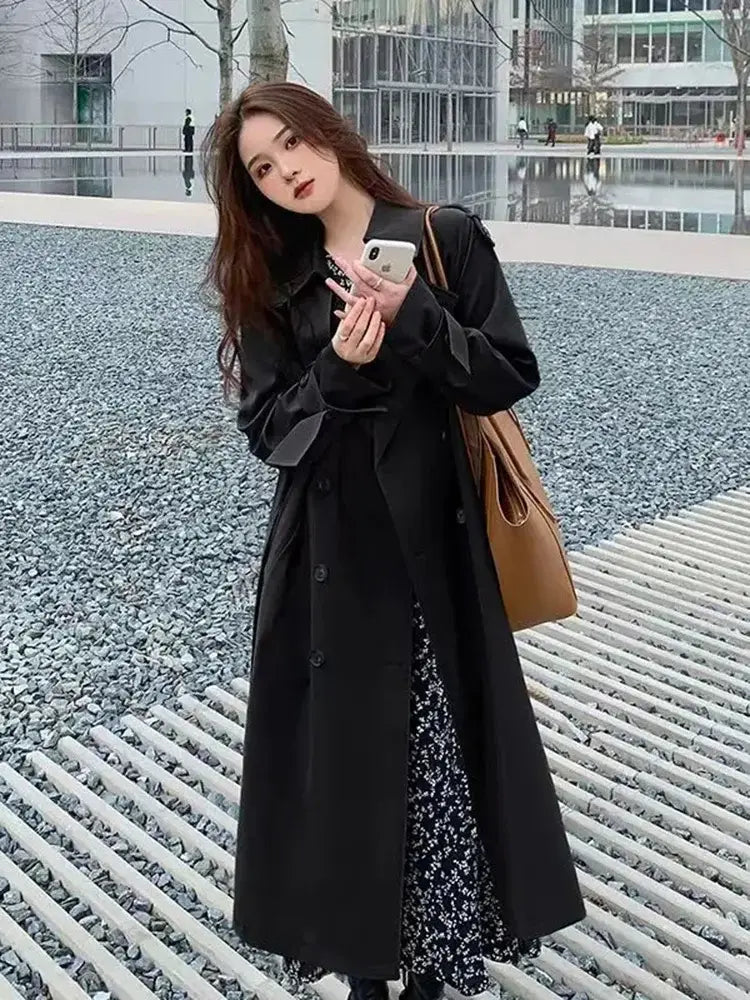 Black trench coat with a classic double-breasted design and buttoned front worn over a patterned dress for casual windbreaker use.
