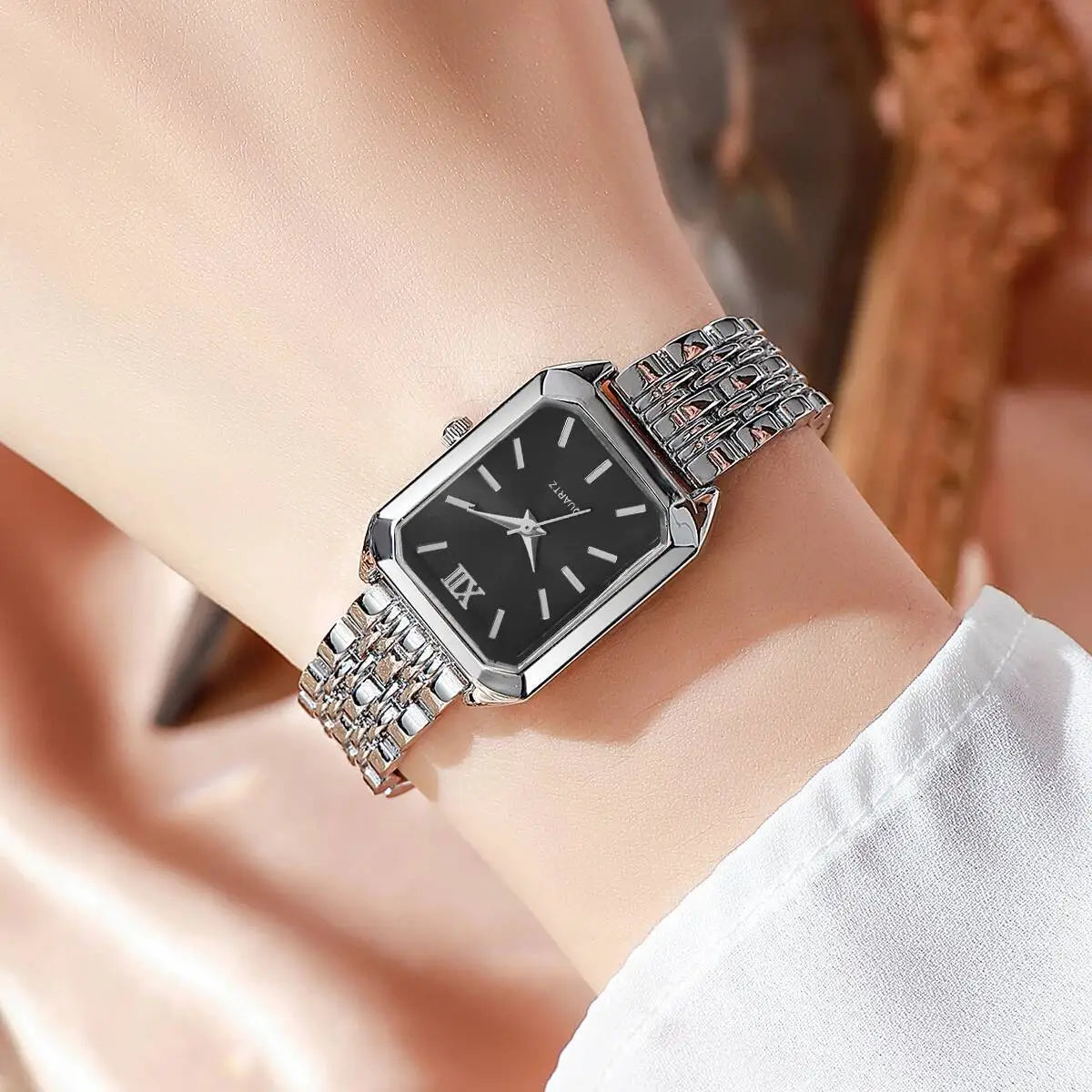 Silver women rectangular quartz watch with a black dial featuring roman numeral hour markers and an intricate silver mesh strap design.