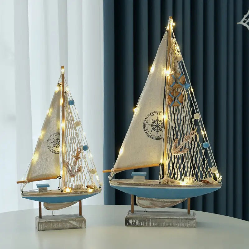 Zwei Deko-Modelle im mediterranen Stil aus Holz mit LED-Licht für Segelboote: Segel in Cremefarbe, blaue Rümpfe und Lichterketten, die durch das Netz geflochten sind, verziert mit Ankern und Muscheln.