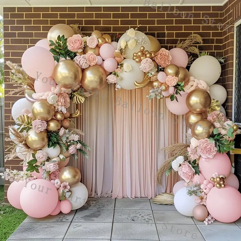 A decorative pink balloon arch kit for wedding and birthday parties featuring metallic gold soft pink and white latex balloons adorned with artificial flowers and greenery.