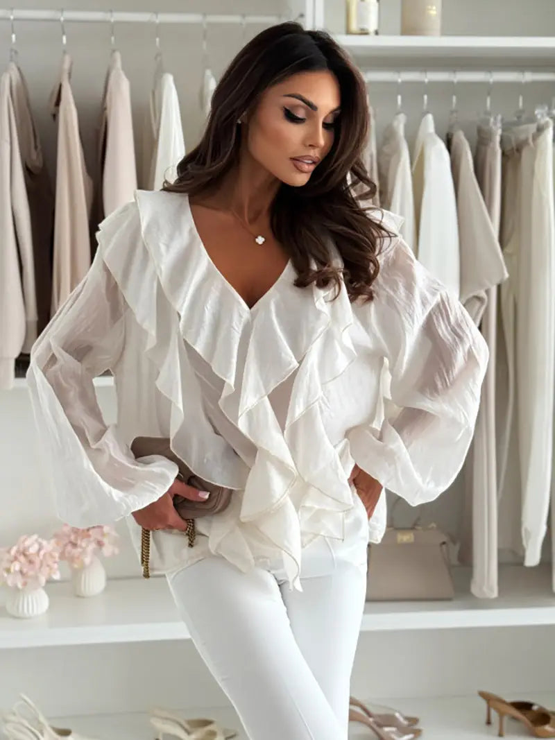 Blouse blanche à encolure en V à volants, manches bouffantes longues transparentes et tissu délicat.
