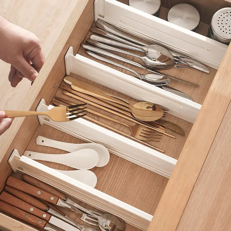 Organisateur de tiroir en plastique blanc avec séparateur extensible en plastique et plusieurs compartiments, destiné à accueillir des ustensiles en argent et en bois.