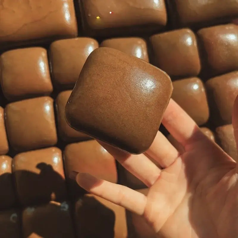 A smooth glossy brown slow rising squishy mini toast fidget toy with a square shape rounded edges and a slightly textured surface.