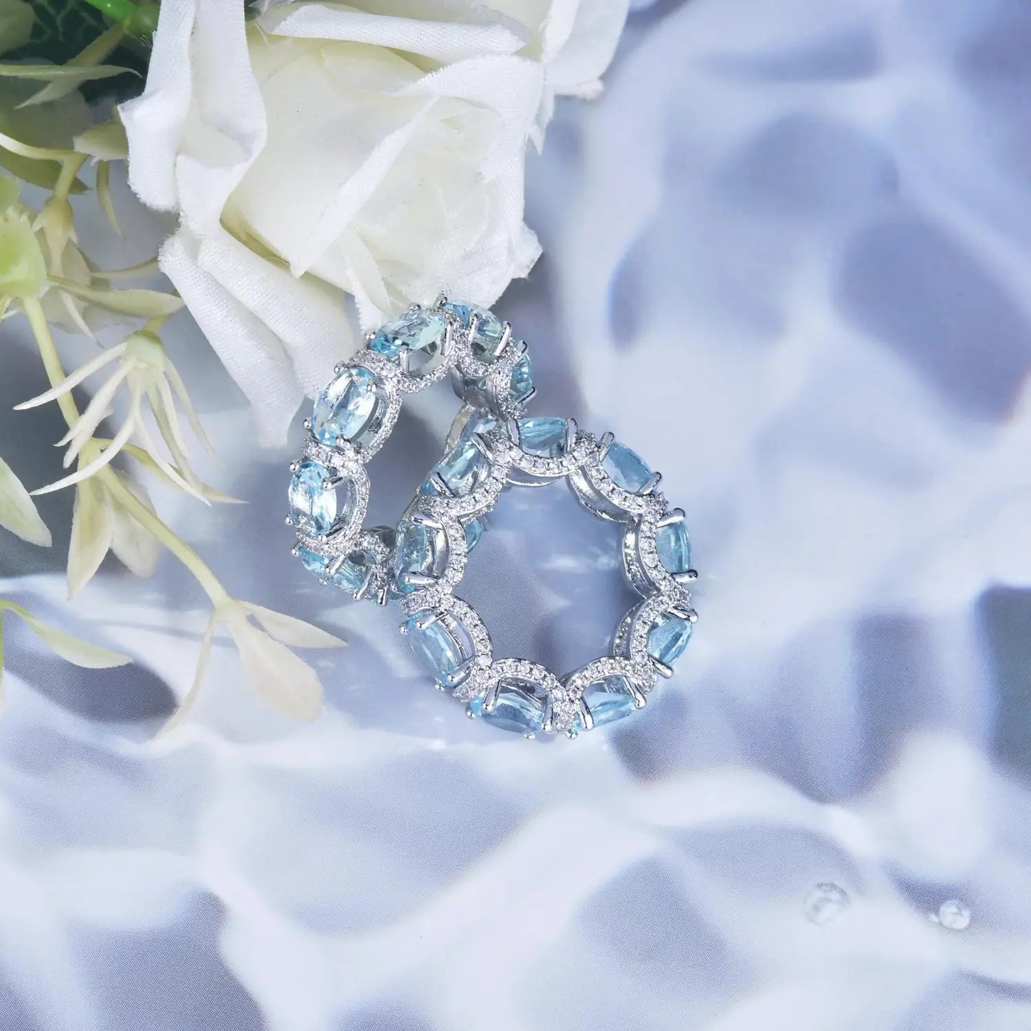 A pair of elegant silver-toned bridal rings with oval-cut sky blue aquamarine crystals surrounded by a halo of sparkling clear stones.