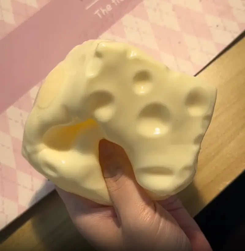 Un jouet à mâcher et à malaxer en forme de fromage, de couleur jaune pâle, conçu pour soulager le stress, avec texture molle et finition brillante, ainsi qu’avec des orifices caractéristiques, conçu pour apaiser le stress lié au jouet.
