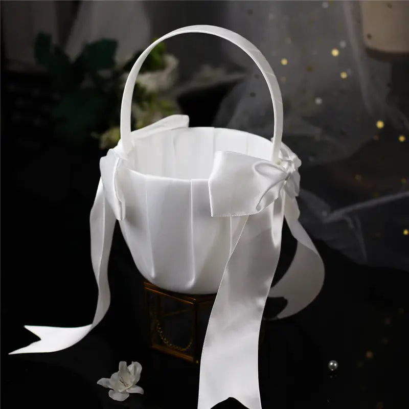 Panier de demoiselle d’honneur en satin blanc avec une anse assortie et un nœud perlé décoratif.